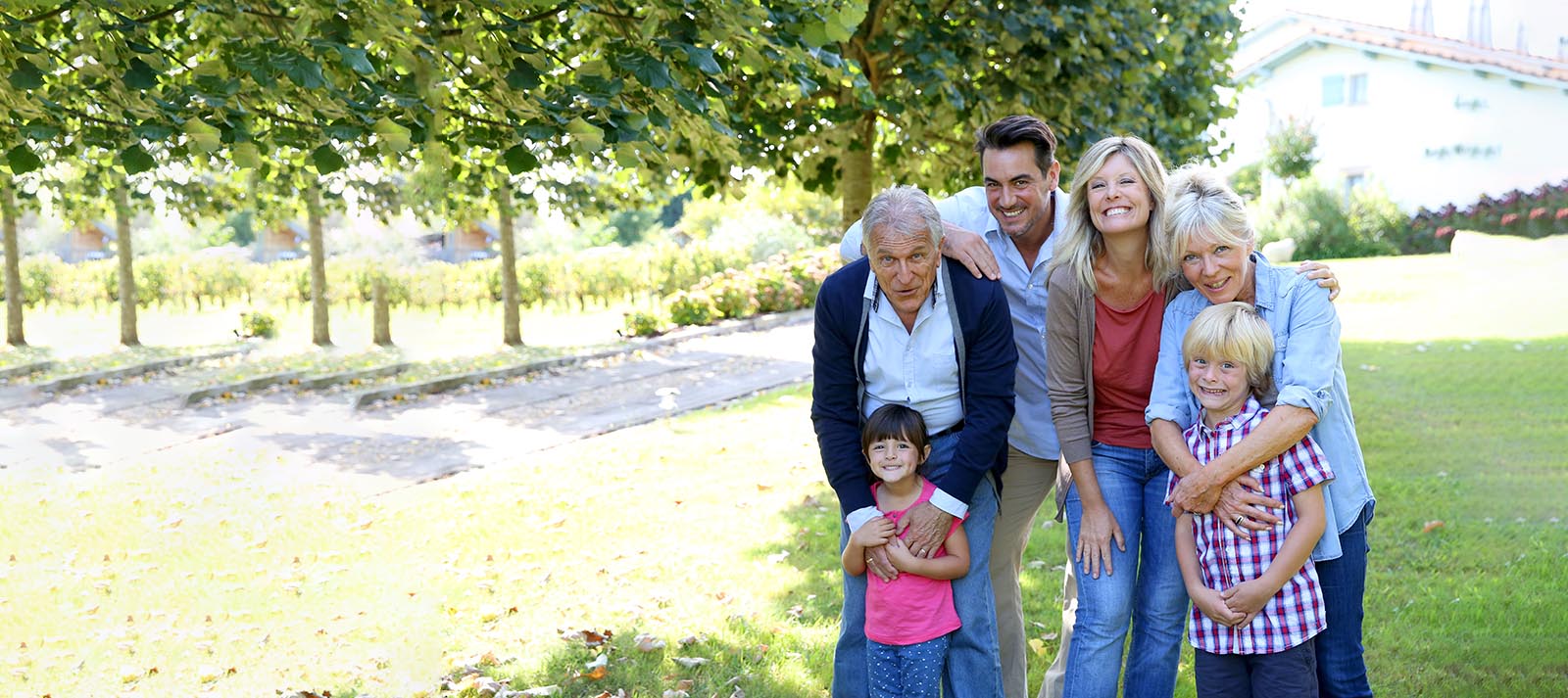A family of four posing together for a photo in front of a tree, with the older couple embracing their adult children.