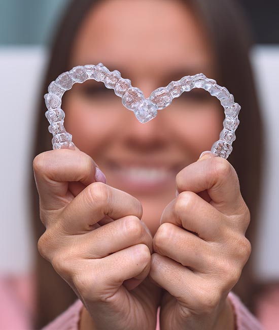 A smiling individual holding a transparent heart-shaped object with clear braces.